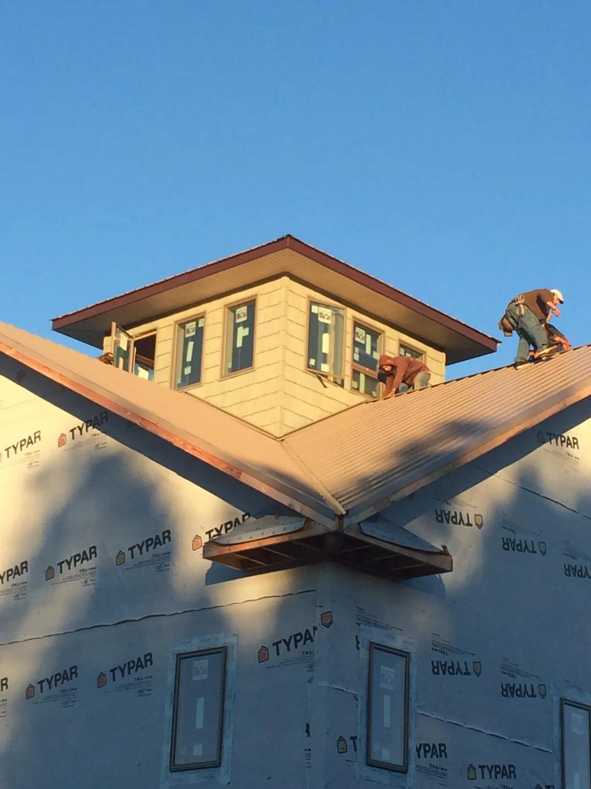 Roofers working around a rooftop cupola on a new metal roof at sunset — Roof Waterproofing in Cumberland by Roofing Brothers